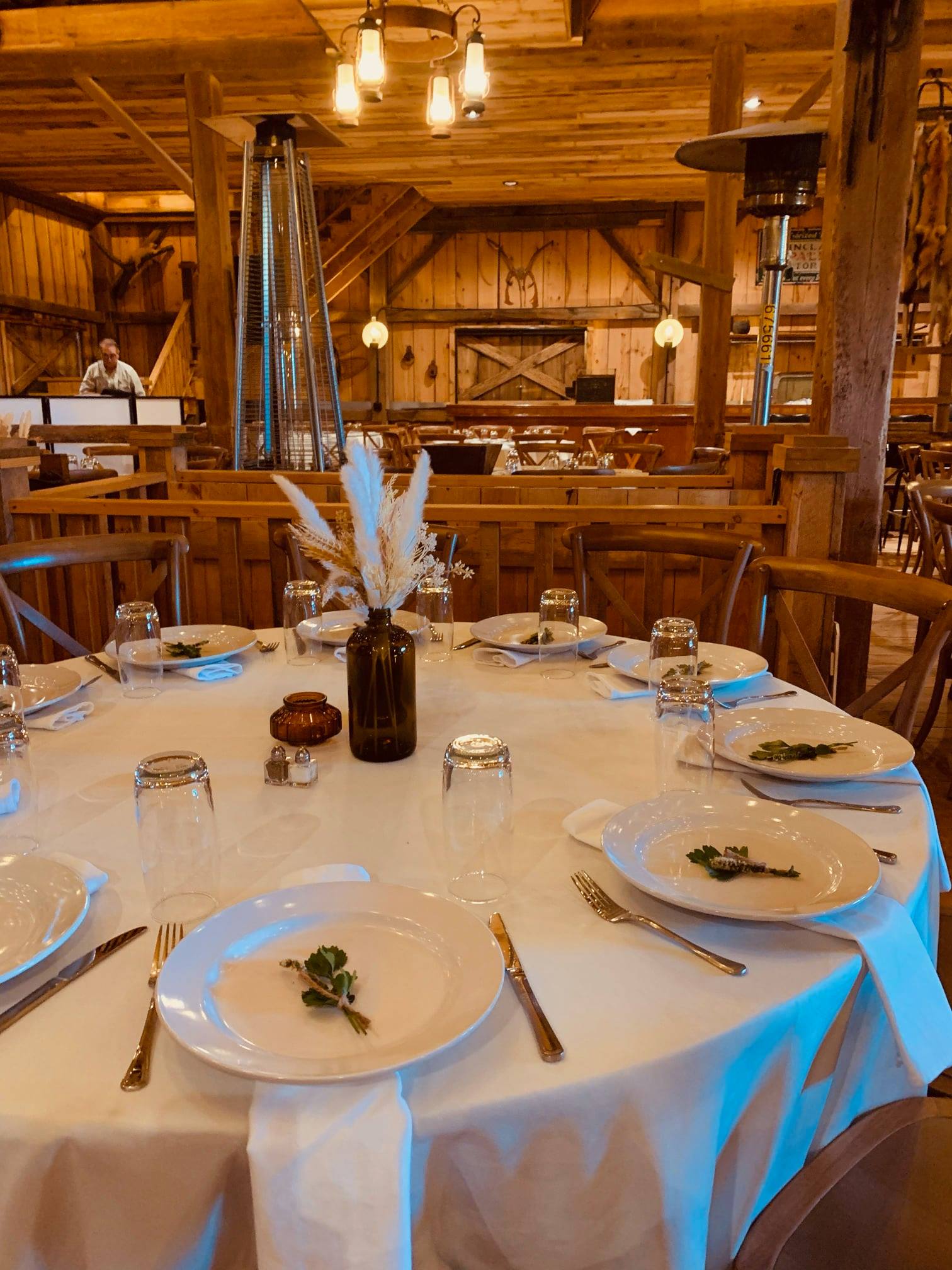 The image depicts a rustic, well-lit eating establishment. The tables are made of solid wood and are set with bowls of gre...